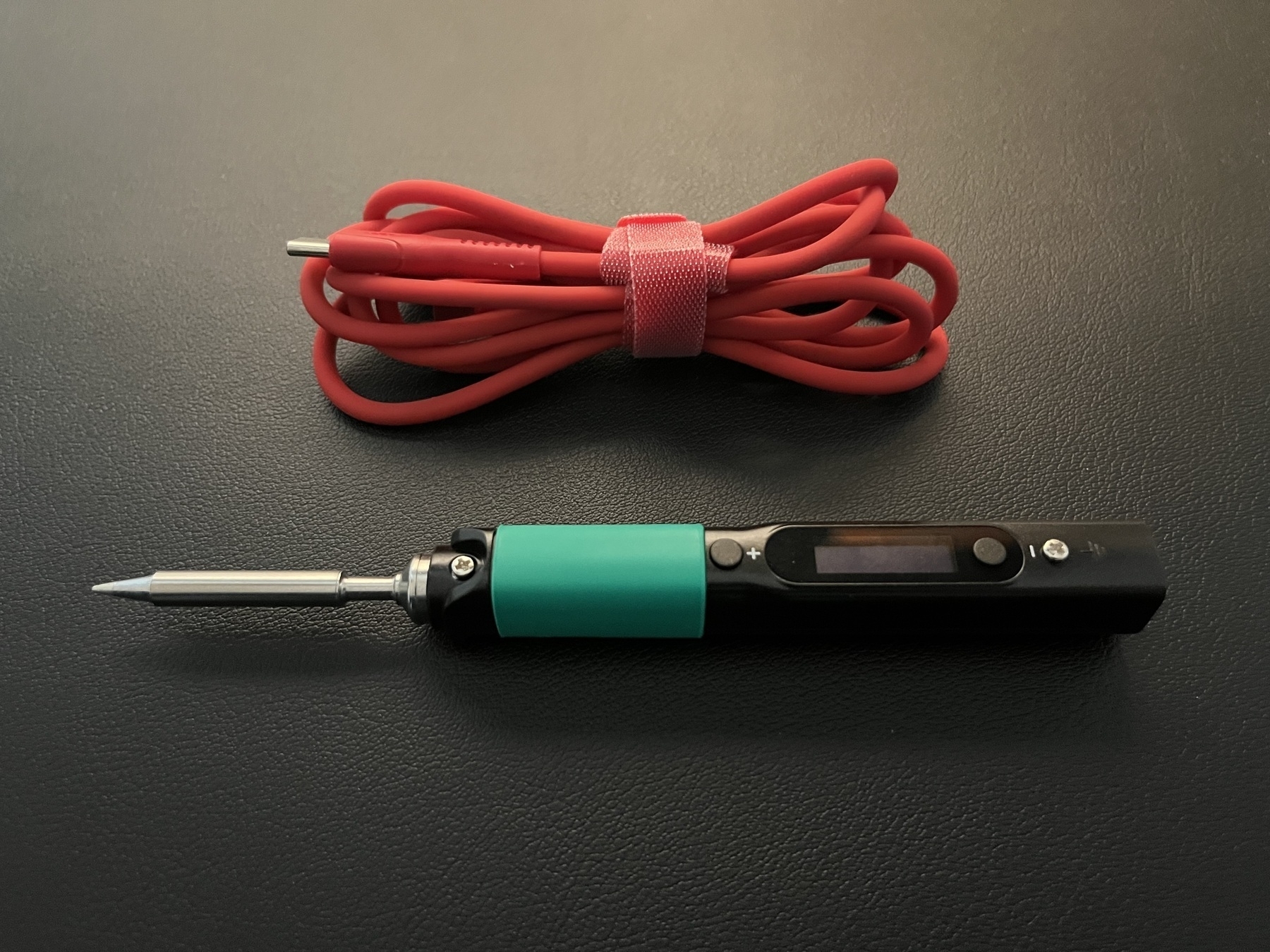 Photo of a soldering iron sitting on a black pleather mat.